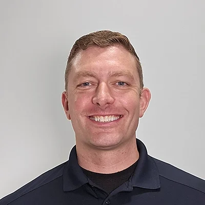 Brian Horne smiling in front of a grey wall.